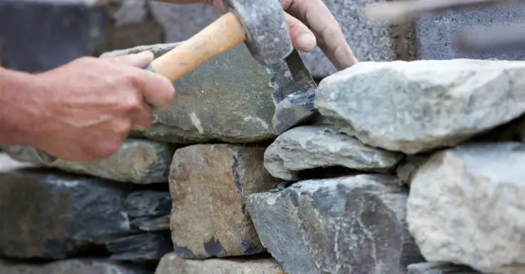 Un homme avec un marteau construit un muret en pierres sèches