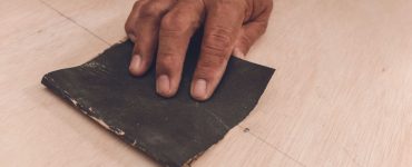 Main d’un homme utilisant du papier de verre pour aplanir la surface d'une feuille de contreplaqué avant de peindre