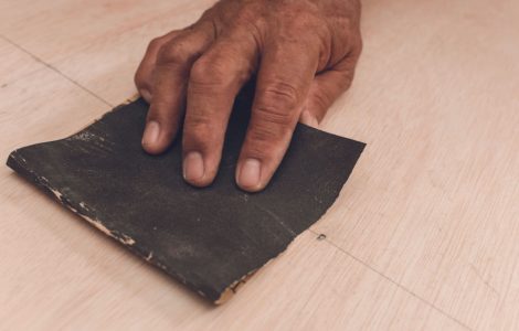 Main d’un homme utilisant du papier de verre pour aplanir la surface d'une feuille de contreplaqué avant de peindre