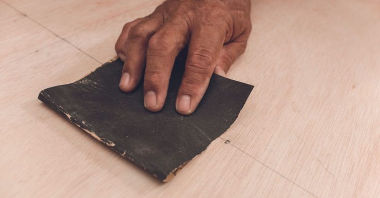 Main d’un homme utilisant du papier de verre pour aplanir la surface d'une feuille de contreplaqué avant de peindre