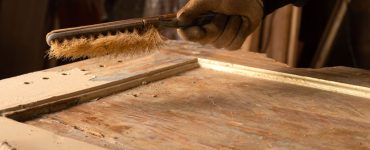 Zoom sur la main d’un homme nettoyant une vieille porte en bois avec une brosse