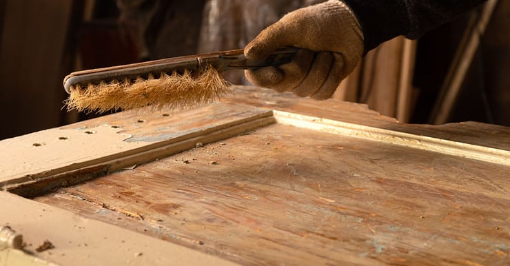 Zoom sur la main d’un homme nettoyant une vieille porte en bois avec une brosse