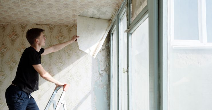 Un homme sur un escalier retire le papier peint du plafond