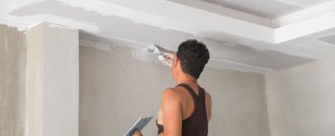 Un homme rénovant le plafond avec du plâtre à l'aide de sa truelle
