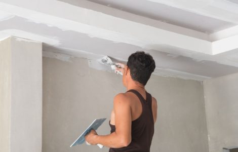 Un homme rénovant le plafond avec du plâtre à l'aide de sa truelle