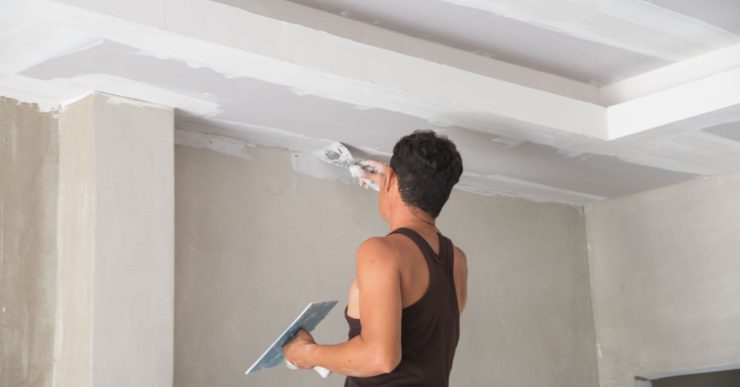 Un homme rénovant le plafond avec du plâtre à l'aide de sa truelle