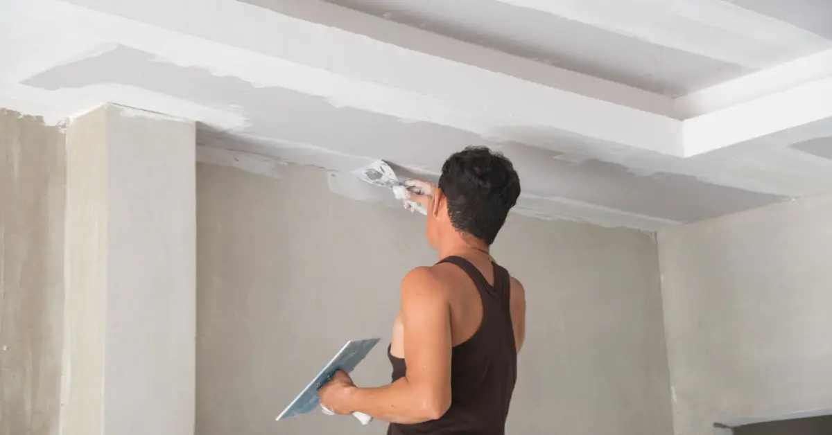 Un homme rénovant le plafond avec du plâtre à l'aide de sa truelle