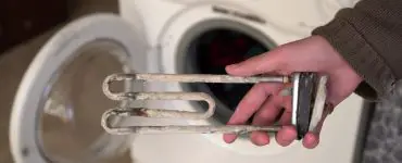 Focus sur la main d’une personne montrant le dépôt de calcaire sur la résistance du lave-linge