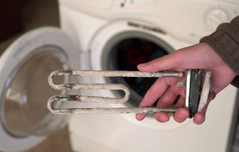 Focus sur la main d’une personne montrant le dépôt de calcaire sur la résistance du lave-linge