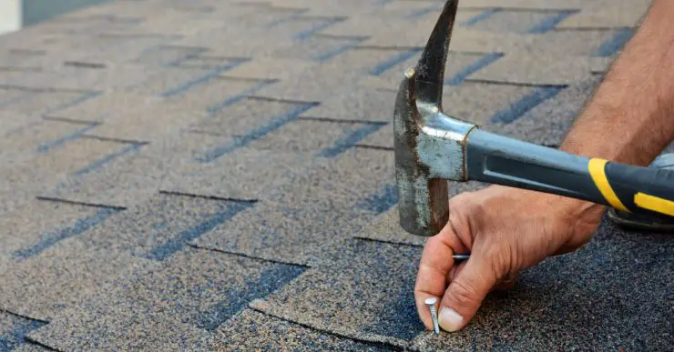Zoom sur les mains d'un homme installant des bardeaux de toit en bitume avec un marteau