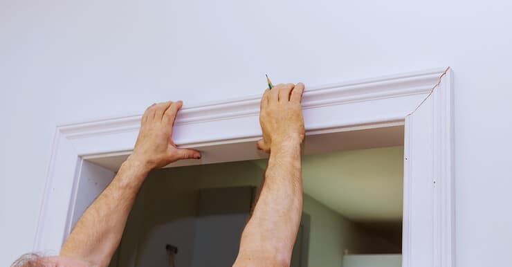 Un homme tient l'encadrement supérieur de la porte, un crayon à la main