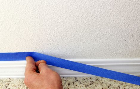 Main d’un homme plaçant un ruban bleu au-dessus des plinthe avant de les peindre