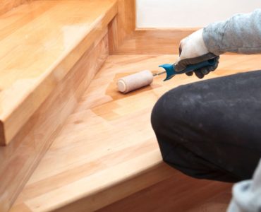 Zoom sur la main d’un homme appliquant du vernis sur un escalier en bois à l’aide d’un rouleau