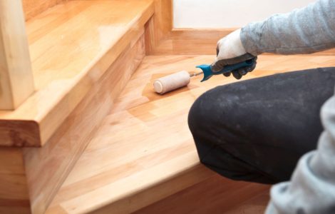 Zoom sur la main d’un homme appliquant du vernis sur un escalier en bois à l’aide d’un rouleau