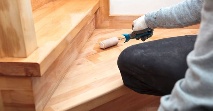 Zoom sur la main d’un homme appliquant du vernis sur un escalier en bois à l’aide d’un rouleau