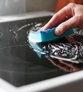 Zoom sur la main d'un homme nettoyant une plaque de cuisson avec une éponge