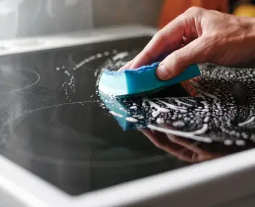 Zoom sur la main d'un homme nettoyant une plaque de cuisson avec une éponge