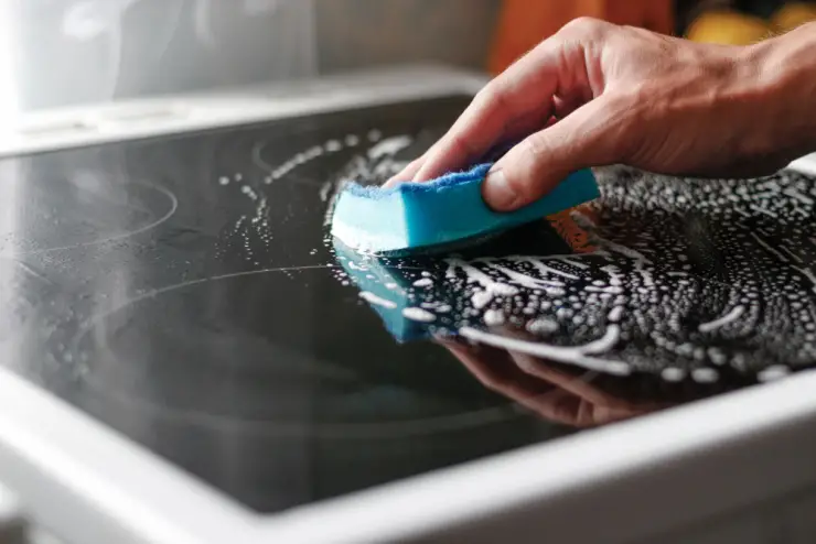 Zoom sur la main d'un homme nettoyant une plaque de cuisson avec une éponge