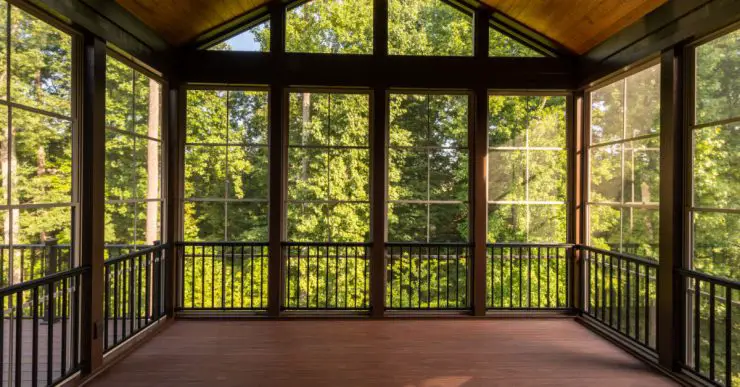 Vue sur la forêt à travers une grande véranda avec parquet en bois