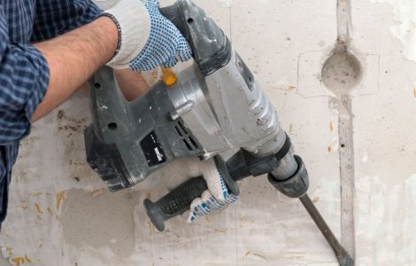 Un homme réalise une saignée dans un mur à l’aide d’un marteau perforateur