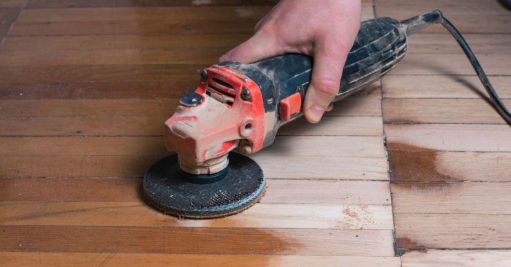 Zoom sur la main d’un homme en train de poncer le parquet avec une ponceuse électrique