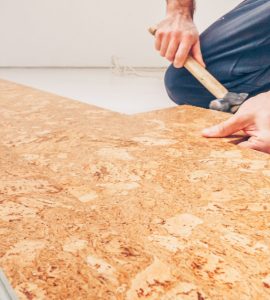 Un homme installe un sol en liège à l'aide de son marteau