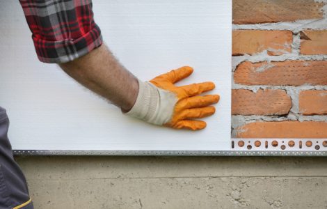 Un homme en gants jaunes installe de l'isolant thermique en polystyrène sur un mur de briques