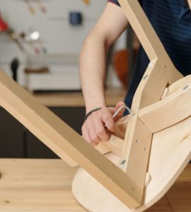 Vue sur un homme en train de resserrer les boulons de fixation d’une chaise en bois