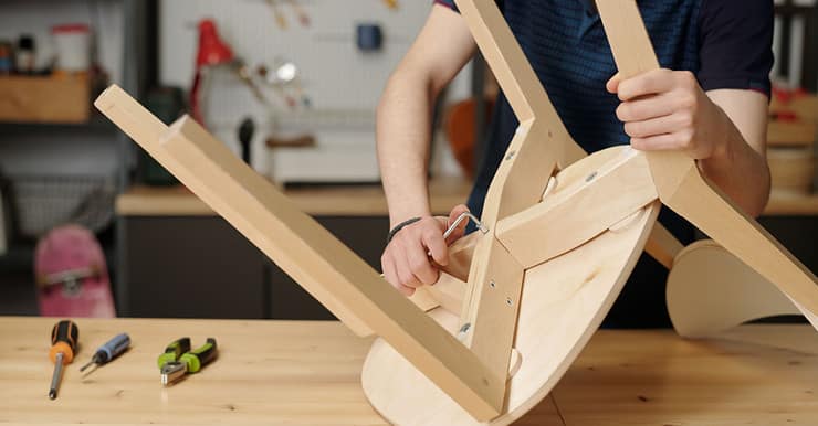 Vue sur un homme en train de resserrer les boulons de fixation d’une chaise en bois