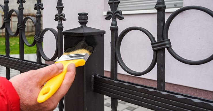 Main d’un homme utilisant un pinceau jaune pour peindre une clôture en fer en noir