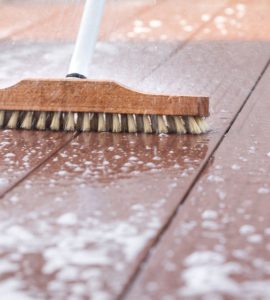 Un homme nettoyant une terrasse avec une brosse et de l'eau savonneuse