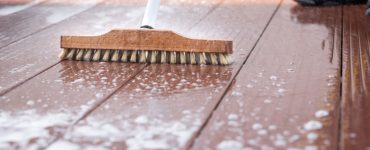 Un homme nettoyant une terrasse avec une brosse et de l'eau savonneuse