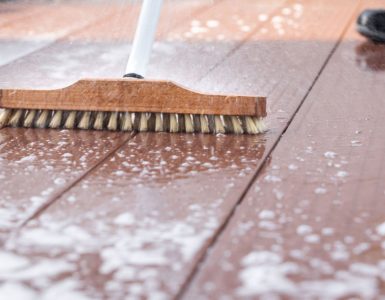 Un homme nettoyant une terrasse avec une brosse et de l'eau savonneuse