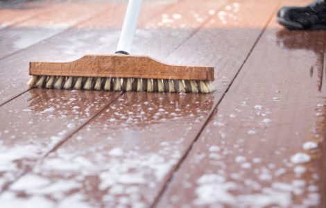 Un homme nettoyant une terrasse avec une brosse et de l'eau savonneuse