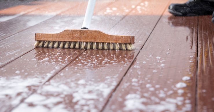 Un homme nettoyant une terrasse avec une brosse et de l'eau savonneuse