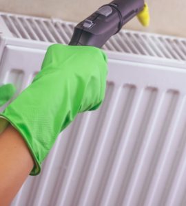 Une femme en gants verts nettoyant son chauffage avec un nettoyeur à vapeur