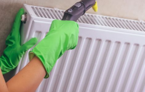 Une femme en gants verts nettoyant son chauffage avec un nettoyeur à vapeur