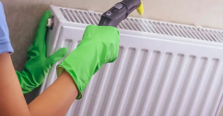 Une femme en gants verts nettoyant son chauffage avec un nettoyeur à vapeur