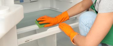 Une femme portant des gants jaunes nettoie l'intérieur du réfrigérateur