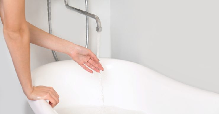 Une femme remplissant la baignoire teste la température de l'eau