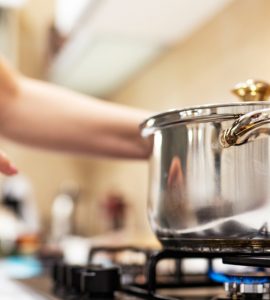 Une femme debout devant une casserole en acier sur une gazinière allumée