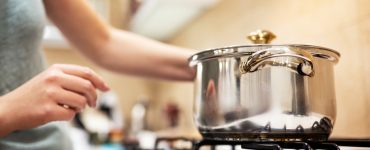 Une femme debout devant une casserole en acier sur une gazinière allumée