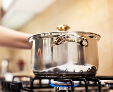 Une femme debout devant une casserole en acier sur une gazinière allumée