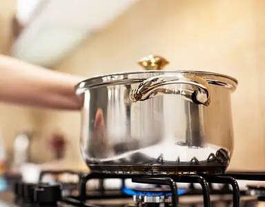 Une femme debout devant une casserole en acier sur une gazinière allumée