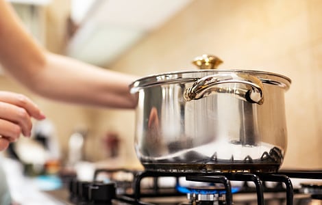 Une femme debout devant une casserole en acier sur une gazinière allumée