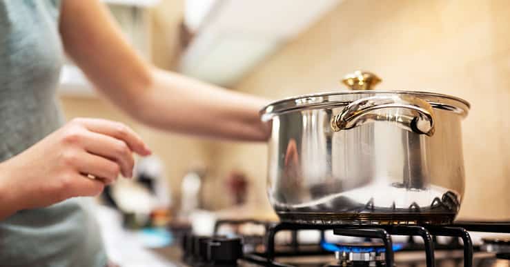 Une femme debout devant une casserole en acier sur une gazinière allumée