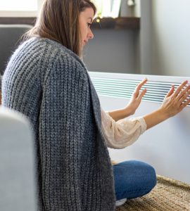 Femme se réchauffant les mains près du chauffage électrique