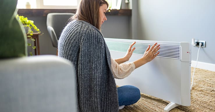 Femme se réchauffant les mains près du chauffage électrique