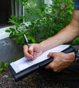 Un homme accroupi près d'une fenêtre prend des notes sur une fiche