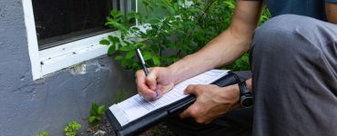 Un homme accroupi près d'une fenêtre prend des notes sur une fiche